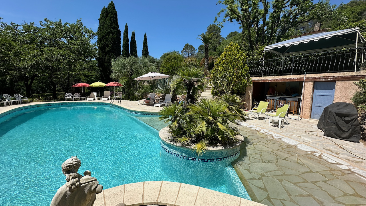 Vue de la piscine avec parasols et végétation méditerranéenne